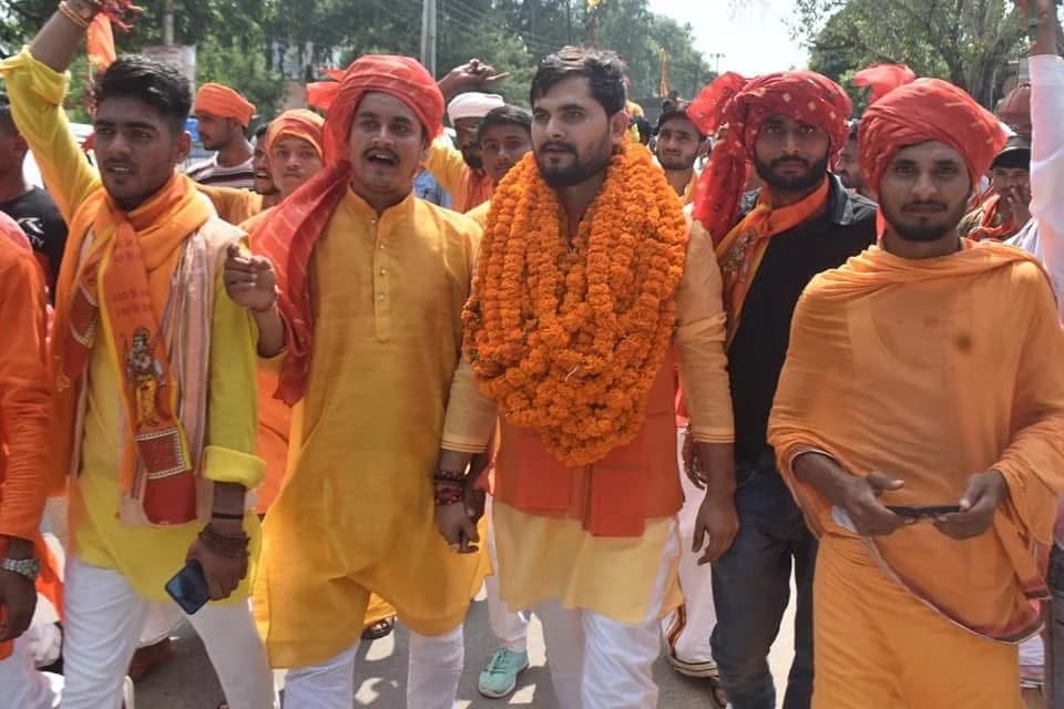 खुले स्थान पर सभा में माला पहने प्रतिभागियों का समूह।